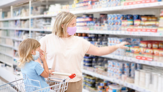  A woman and child wearing masks shopping in a grocery store aisle filled with various products.